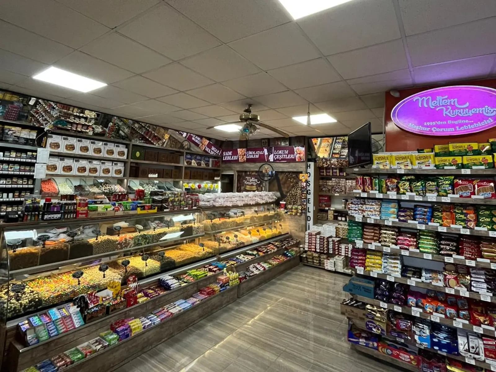 Dükkânın içi: tezgâhta dökme leblebi ve kuruyemiş bölmeleri, raflarda paketli ürünler
